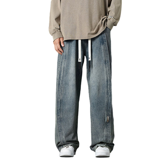 Person wearing a beige sweater and blue jeans on a dark background